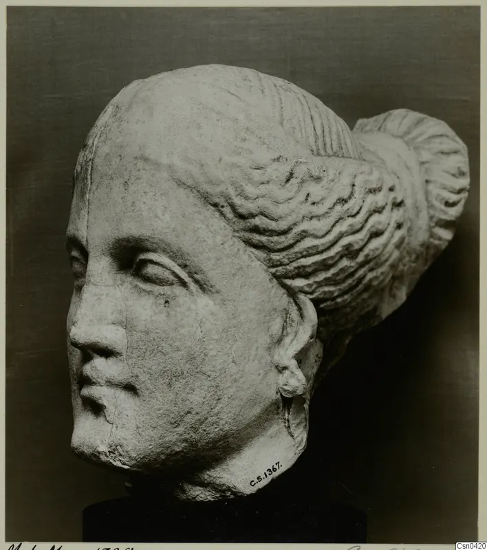 Limestone head of a statue with wavy hair drawn back into a large bun at the back