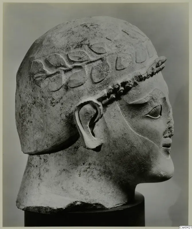 Limestone head in profile with a carved leaf band across the hair, on a dark cylindrical base.