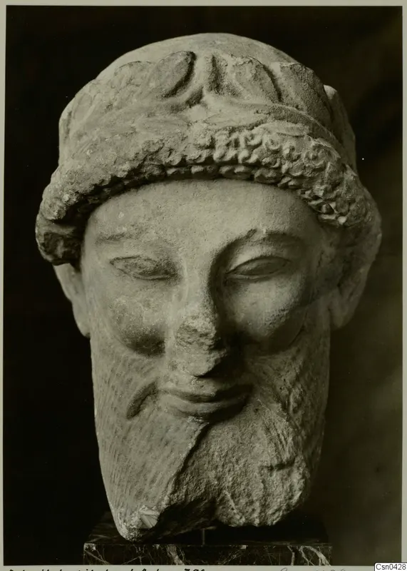 Limestone head of a bearded man with a curled headband, on a dark marble base