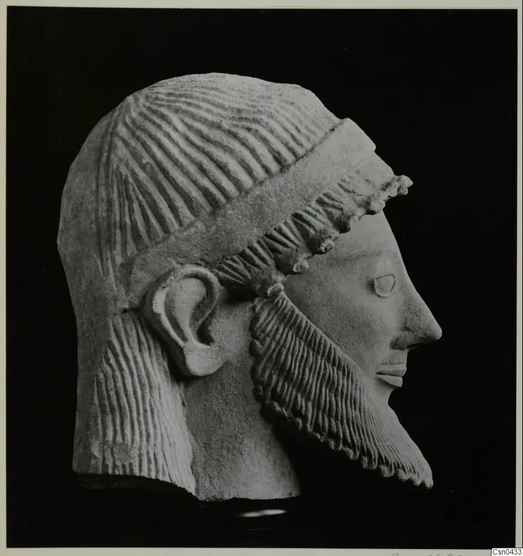 Limestone head of a bearded male sculpture in profile, facing right, with a band across the hair.