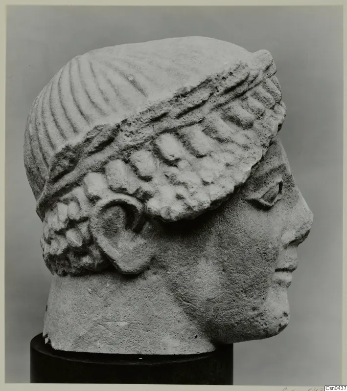 Limestone head of a figure in profile, with a ribbed headdress and curled hair, on a dark stand
