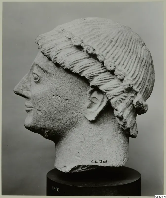 Limestone head of a figure in profile, with ridged hair bound by a band, on a dark stand.