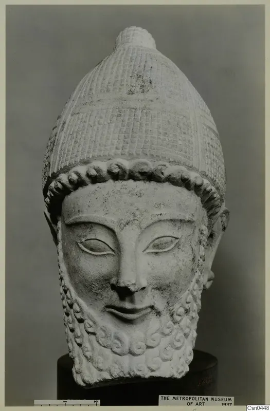 Limestone head of a bearded male figure wearing a tall patterned cap, shown on a dark stand.