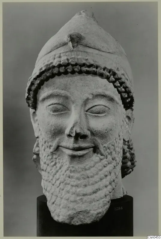 Limestone head of a bearded man in a tall cap, shown frontally on a black cylindrical stand