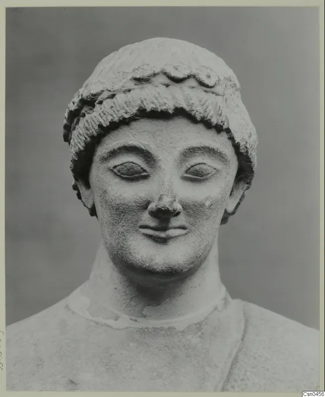 Limestone head of a statue with rows of curls and a band across the forehead, shown from the front.