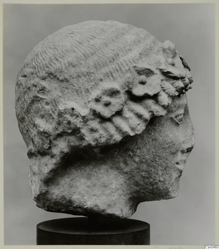 Limestone head sculpture in side view, face turned to the right, on a dark cylindrical stand.