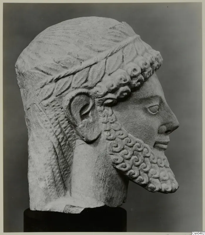 Limestone head with a curled beard and leafy band in the hair, shown in profile on a dark base