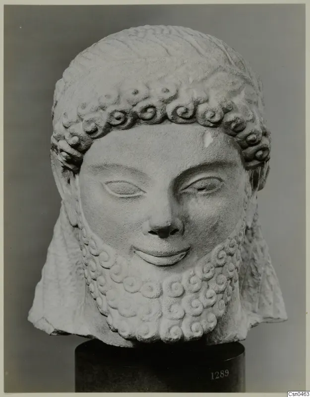Limestone head of a bearded statue with curled hair and beard, on a dark stand
