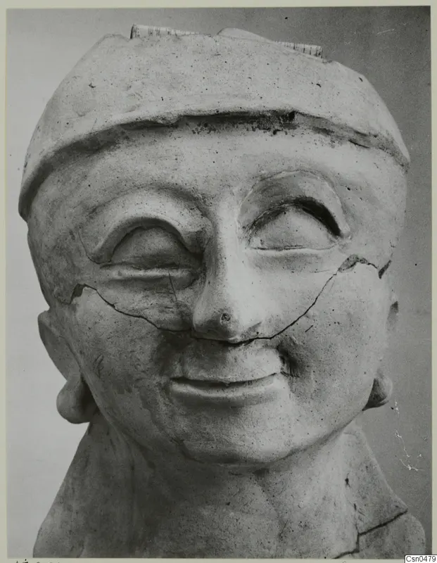 Terracotta head of a figure with a flat cap, large heavy-lidded eyes and a broad smile, cracked across the face