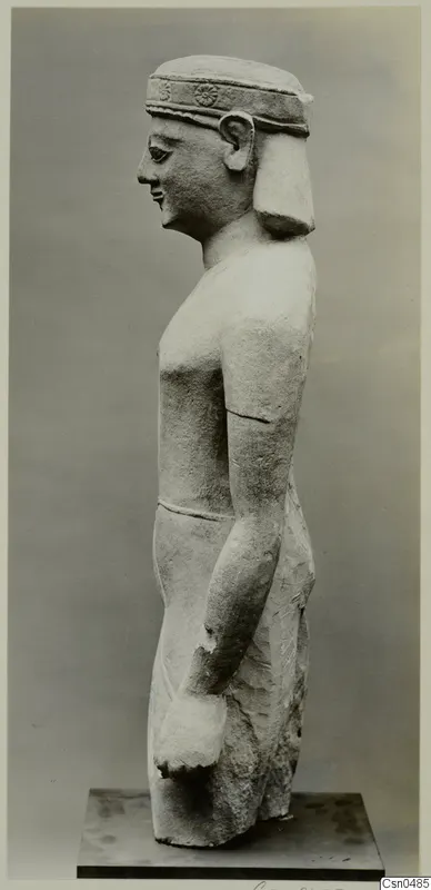 Limestone statue of a standing figure seen in profile, wearing a headband, with arms held at its sides.