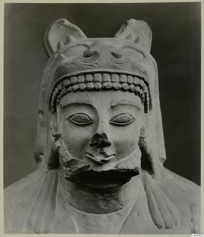 Limestone sculpture of a bust wearing a headdress with upright projections; the nose and mouth are broken away.