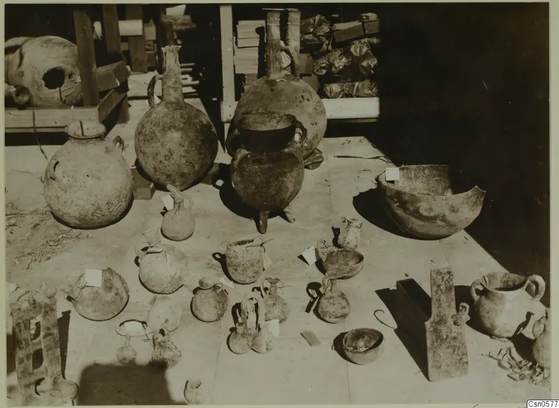Pottery jars, jugs and bowls set out together on a floor, with paper tags tied to several of the pieces