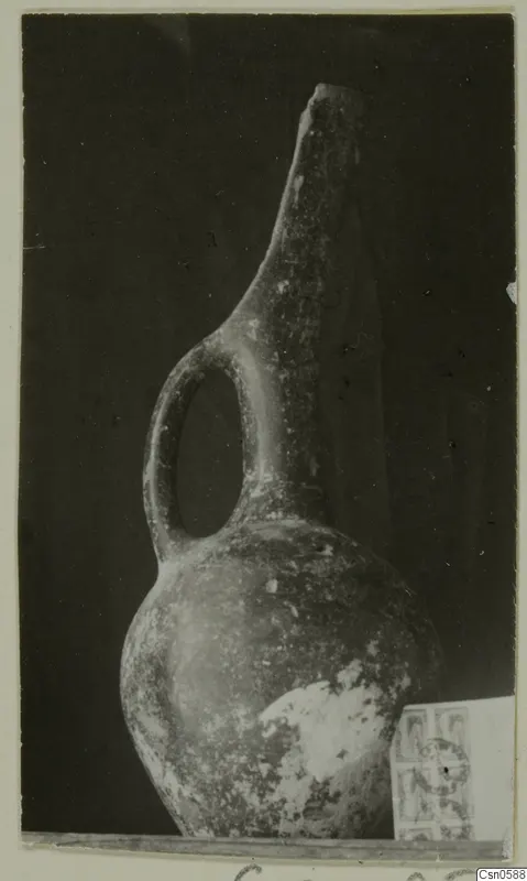Jug with a tall narrow neck and a single loop handle, photographed against a dark background