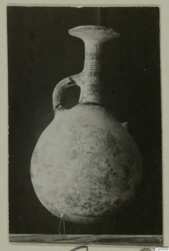 Pottery jug with a round body, loop handle and incised chevron pattern on a dark background