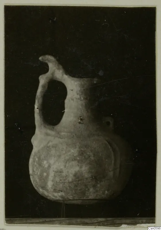 Pottery jug with a strap handle and pinched spout, photographed against a dark background