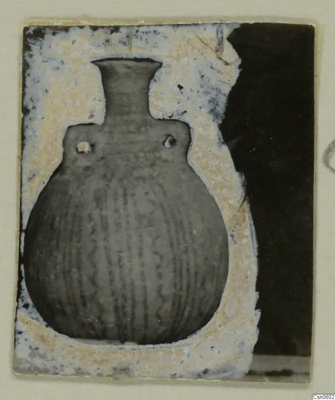 Globular pot with a tall narrow neck, two small lugs on the shoulder and vertical grooves on the body, shown in a window-cut card mount