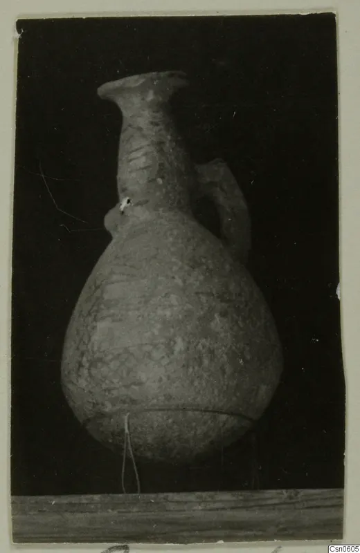 Pottery vessel with a flared rim, single handle and painted pattern, photographed against a black background