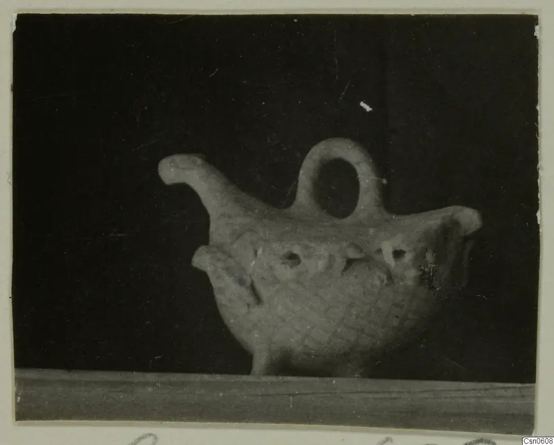 Pottery vessel with a loop handle, a raised spout and a patterned body, shown against a dark background.