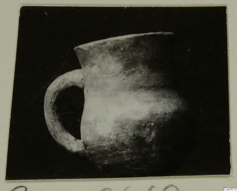 Pottery jug with a flared rim and a single loop handle, shown against a dark backdrop.