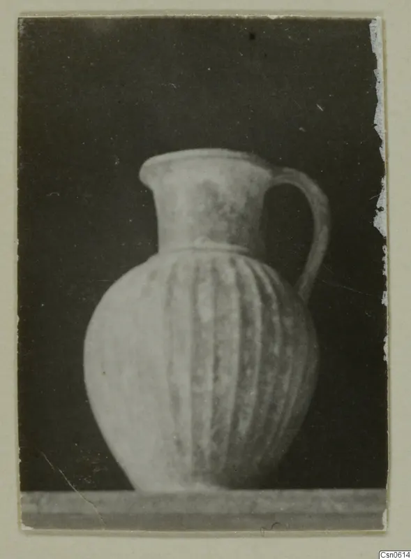 Jug with vertical ribbing on its body and a single loop handle, photographed against a dark background.