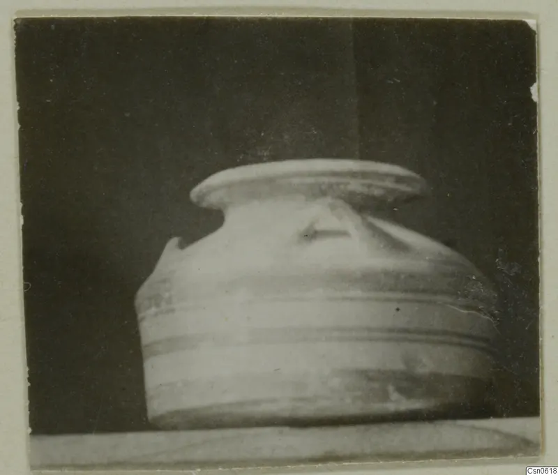 Rounded pottery vessel with horizontal grooves around the body and a broad flat rim, on a pale surface