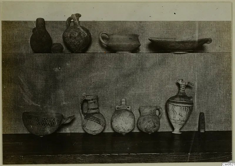 Several pottery vessels, some painted, arranged on two shelves against a cloth backdrop.