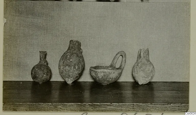 Four pottery vessels standing in a row on a wooden shelf, including a bowl with a loop handle.