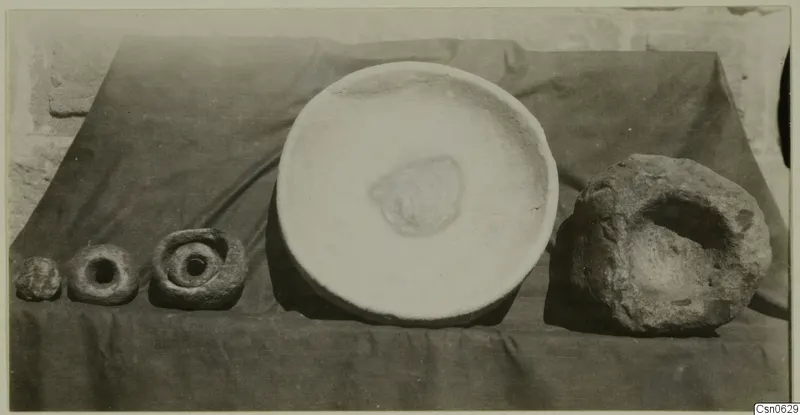 Stone bowl at centre, with four other stone objects laid out on a draped dark cloth against a stone wall.