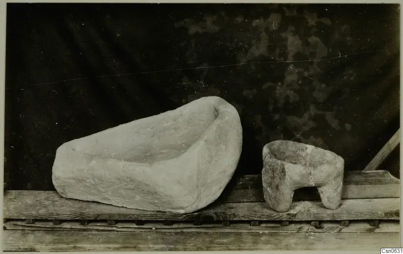 Two stone vessels on a wooden shelf: a large shallow trough and a small bowl standing on short feet