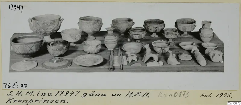 Clay bowls, jugs, lids and small figurines arranged on a wooden table.