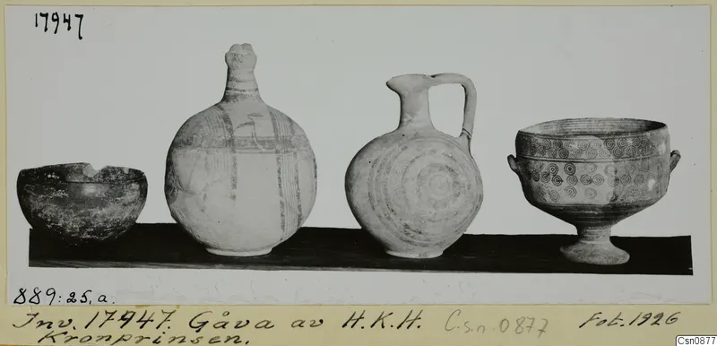 Four painted pottery vessels on a dark board: a bowl, a tall striped bottle, a jug with a loop handle and a footed bowl.