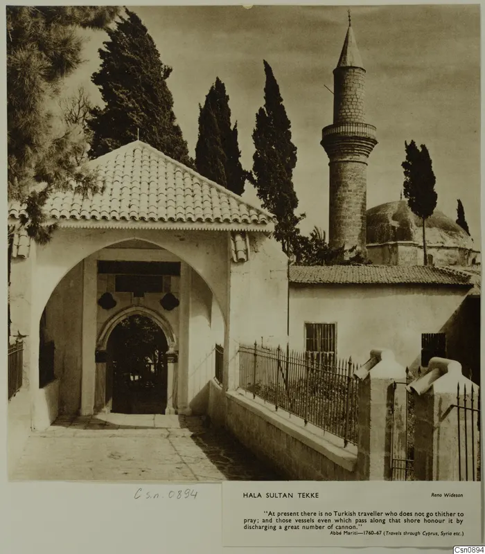 Hala Sultan Tekke: whitewashed arched gateway with a tall stone minaret and cypress trees behind