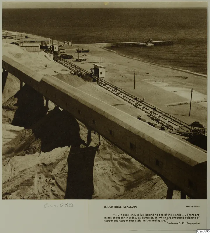 Industrial seascape: a long concrete conveyor on tall supports runs down a beach to a pier extending into the sea.