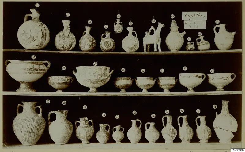 Pottery jugs, flasks and bowls from Lapithos Markides T.2, arranged in three rows on shelves