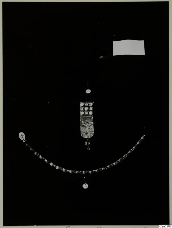 Necklace of beads and a rectangular inlaid plaque with a pendant, laid out on a black background