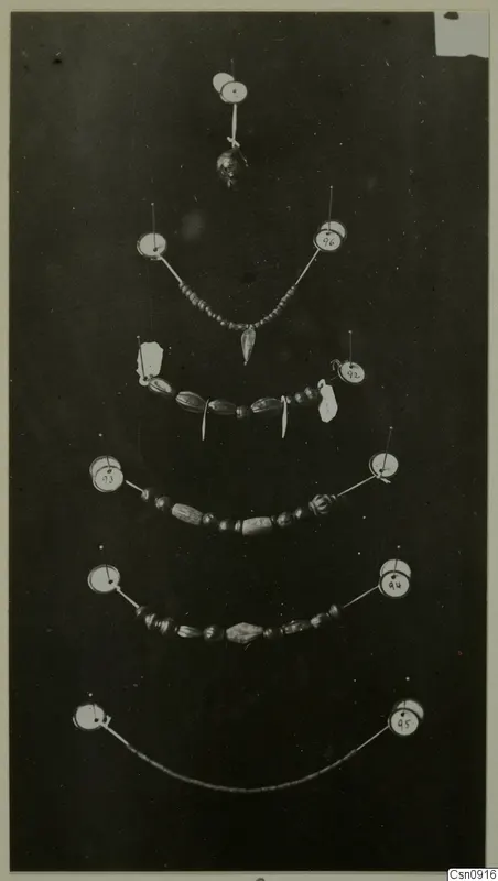 Several strings of beads and a small pendant pinned out on a dark background, each with a round number label.