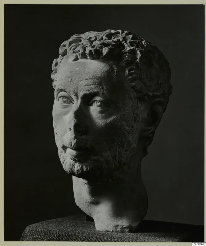 Carved stone male head with curly hair and a short beard, photographed against a dark background.