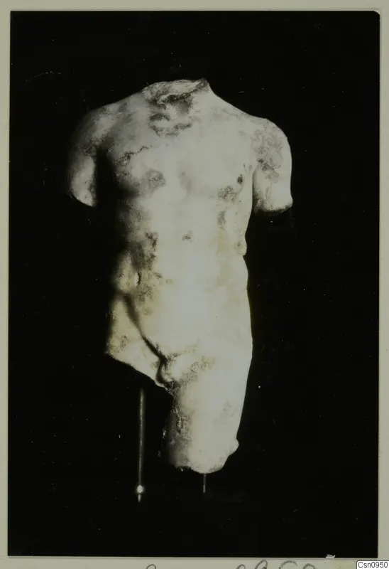 Pale stone torso of a male statue, head and arms missing, shown on a thin stand against a black background