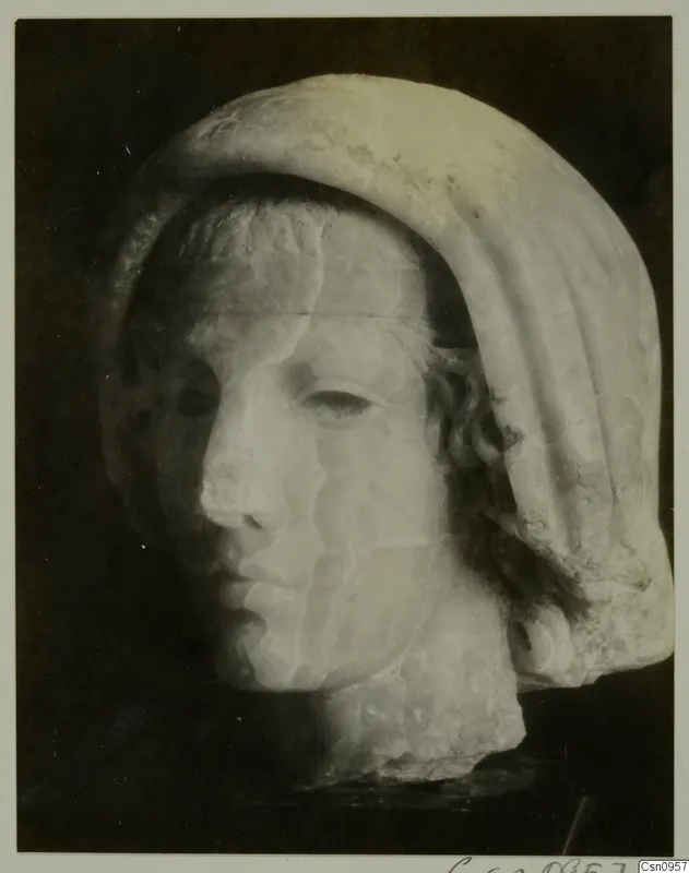 Stone head of a female figure with a draped veil, face turned to the left, against a dark background