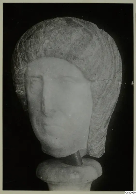 Carved stone head of a figure with layered hair, mounted on a round base, photographed against a black background.