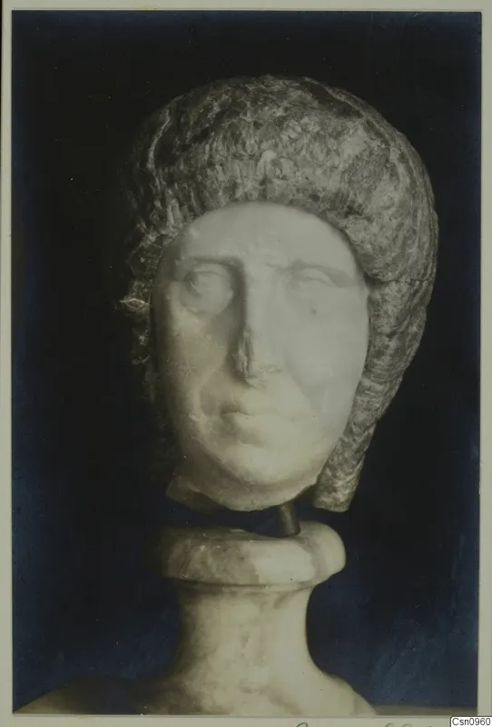 Marble head of a woman with a layered hairstyle, mounted on a carved base against a dark background.