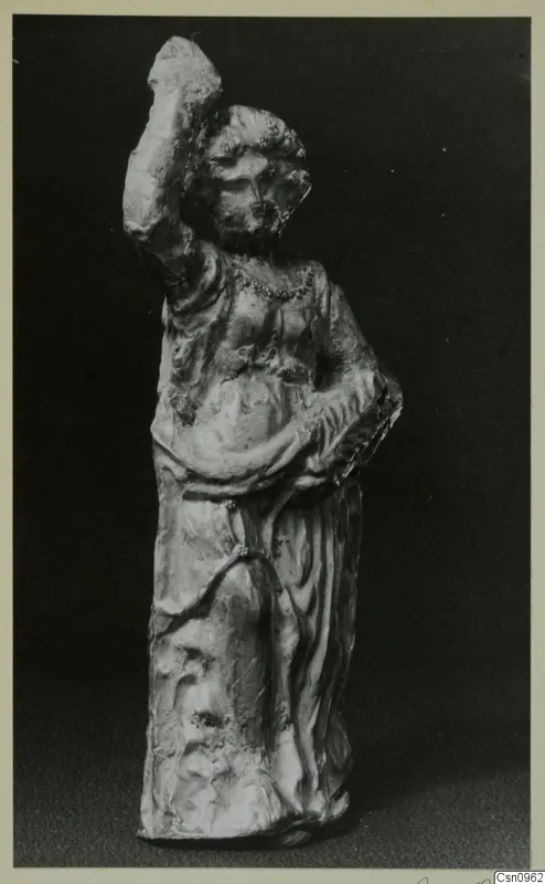 Standing statue of a figure in a long draped garment, one arm raised high, photographed against a dark background