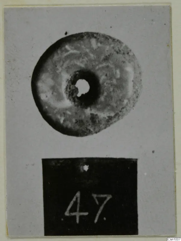 Perforated stone disc with a central hole, photographed above a black number label.