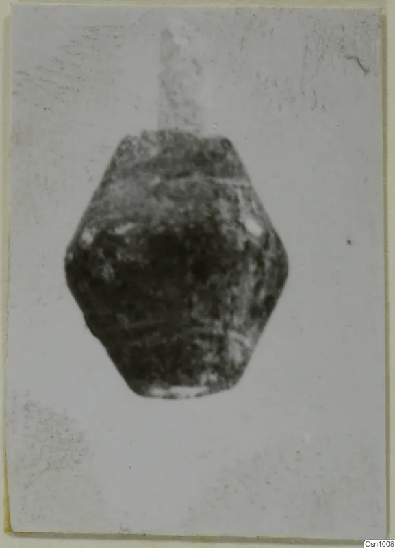 Dark stone bead from Amathus, squat and faceted, shown centred on a pale card