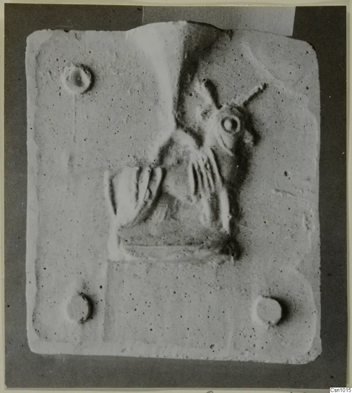 Carved stone relief of a figure on a rectangular stone slab with four small round holes near its corners