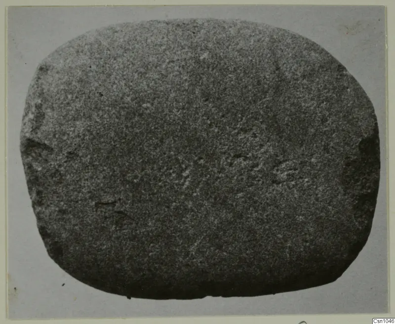 Rounded grey stone object with faint incised marks, photographed flat against a grey backdrop.