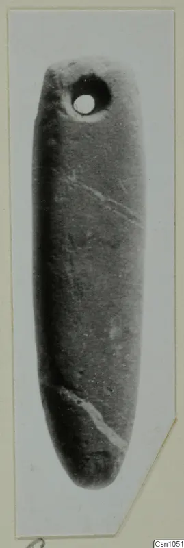 Elongated smooth stone object with a drilled hole near one end, photographed upright on a card mount