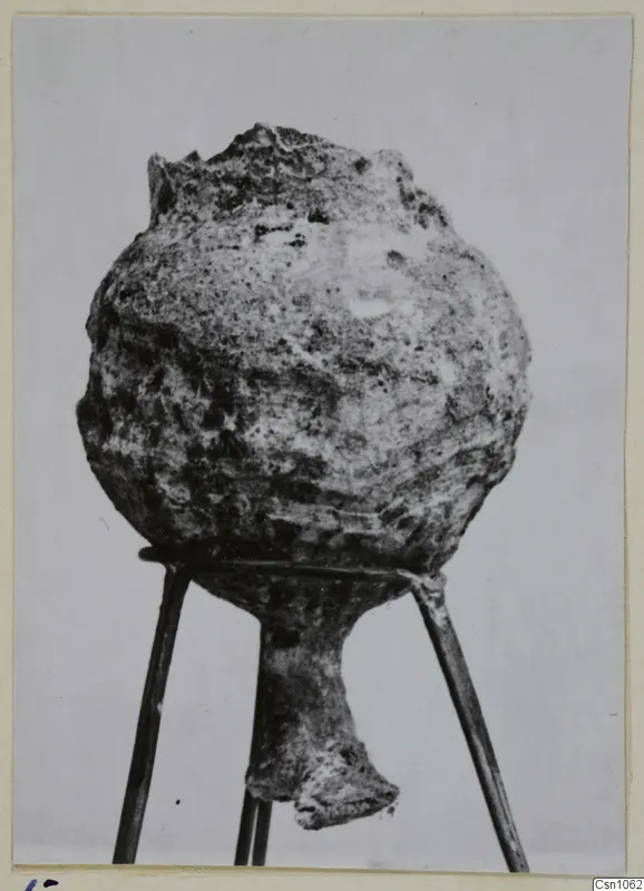 Encrusted rounded vessel with a broken rim and narrow foot, shown on a three-rod stand, from Enkomi