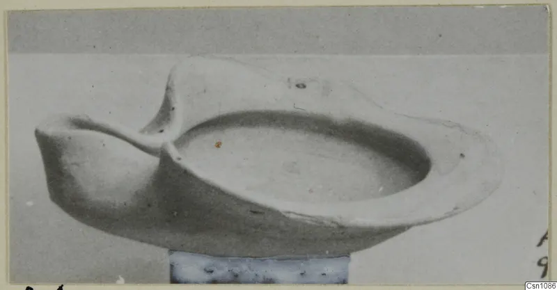 Terracotta lamp with a shallow open bowl and a pinched spout to the left, shown on a stand