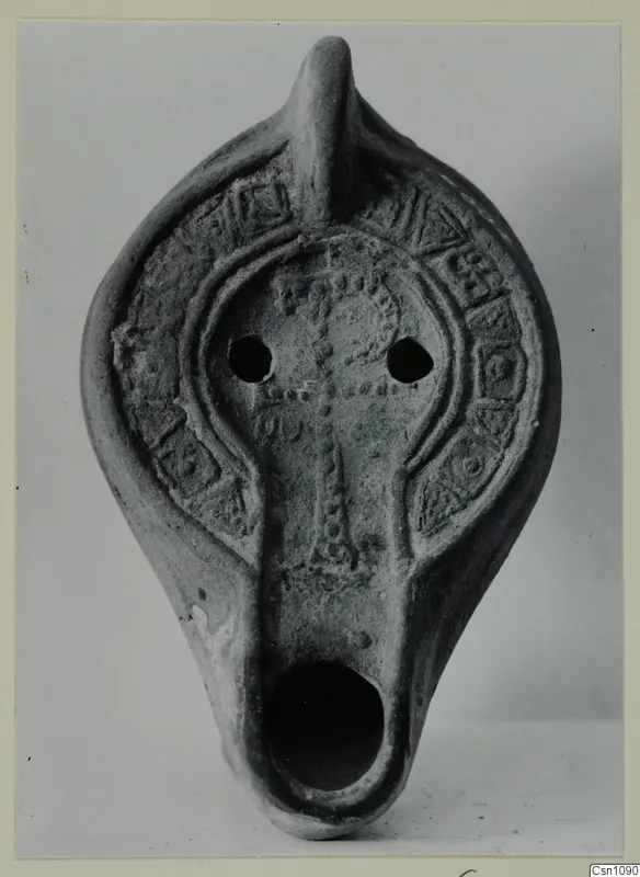 Terracotta oil lamp with a raised cross and rows of dots on the upper surface, seen from the front.
